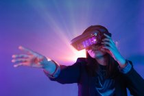 Mulher irreconhecível com braço estendido usando fone de ouvido VR enquanto explora a realidade virtual sob luz de néon azul — Fotografia de Stock
