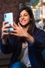 Positive Freiberuflerin macht Selfie und sitzt neben Tisch und Regalen mit Dekorationen, während sie von zu Hause aus arbeitet — Stockfoto