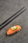 Grand angle de sushi nigiri appétissant avec tranche de saumon sur riz garni d'une fine tranche d'avocat et de fromage à la crème servie près des baguettes — Photo de stock
