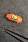 Высокий угол вкусовых суши нигири с ломтиком лосося на рисе, увенчанном тонким ломтиком авокадо и сливочным сыром, подаваемым возле палочек для еды — стоковое фото