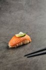Alto ángulo de sushi nigiri sabroso con rebanada de salmón sobre arroz cubierto con rebanada delgada de aguacate y queso crema servido cerca de palillos - foto de stock