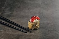 Grand angle de rouleau de sushi japonais frit avec tranches de sésame et de fraise près de bâtonnets de bambou — Photo de stock