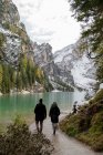 Vue arrière d'un couple méconnaissable en vêtements de dessus marchant le long du lac Lago di Braies dans les hautes terres d'Italie — Photo de stock