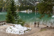 Vista lateral de la pareja en ropa de abrigo caminando a lo largo del lago Lago di Braies en las tierras altas de Italia - foto de stock