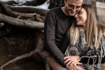 Corpo cheio de casal gentil positivo sentado perto da árvore e abraçando uns aos outros durante o dia romântico na floresta — Fotografia de Stock