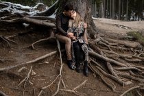 Полное тело позитивной нежной пары, сидящей рядом с деревом и обнимающей и целующей друг друга в течение романтического дня в лесу — стоковое фото