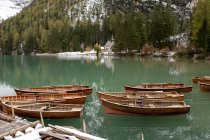 Cenário de barcos de madeira ancorados em calmo lago ondulante cercado por montanhas nevadas e árvores coníferas — Fotografia de Stock