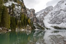 Picturesque scenery of Lago di Braies lake surrounded by evergreen woods and mountains covered with snow — Stock Photo