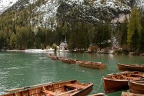 Декорації дерев'яних човнів, облаштованих на спокійному розпалі озера в оточенні засніжених гір і хвойних дерев — стокове фото