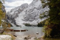 Paesaggio di barche in legno ormeggiate su un lago calmo increspato circondato da montagne innevate e conifere — Foto stock