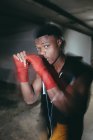 Jovem forte esportista afro-americano no boxe envolve mão trabalhando e olhando para a câmera na construção — Fotografia de Stock