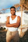 Jeune mâle afro-américain masculin en maillot de corps debout près de la plate-forme et regardant caméra contre maison — Photo de stock