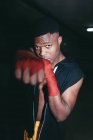 Joven deportista afroamericano fuerte en boxeo mano envuelve el trabajo y mirando a la cámara en el edificio - foto de stock