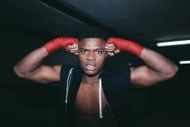 Молодий сильний афроамериканський спортсмен у боксерському ручному обгортку працює і дивиться на камеру в будівлі — стокове фото