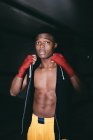 Young strong African American sportsman in boxing hand wraps working out and looking at camera in building — Stock Photo