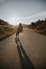 Rückansicht gesichtslose sportliche Frau in trendiger Kleidung fährt Cruiser Board entlang leerer Asphaltstraße in sommerlicher Landschaft an sonnigem Tag — Stockfoto