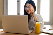 Felice lavoratore autonomo femminile etnico libero professionista in occhiali da vista che lavora su computer portatile a casa — Foto stock