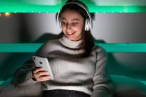 Crop charmante Frau im Pullover Musik mit Kopfhörern hören, während das Handy auf dem Bett surfen — Stockfoto