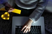 Сверху неопознаваемый подросток в свитере печатает данные кредитной карты на клавиатуре нетбука во время покупок онлайн — стоковое фото