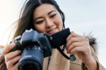Ethnic young happy Asian female photographer shooting photo on professional photo camera on city street — Stock Photo