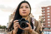 Ethnic Asian female photographer shooting photo on professional photo camera on city street — Stock Photo