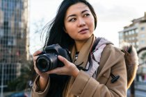 Ethnic young Asian female photographer shooting photo on professional photo camera on city street — Stock Photo