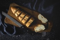 Top view of pieces of white bread near knife and wheat spikes on wooden board — Stock Photo