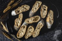 De cima de pão crosty apetitoso perto de picos de trigo e tecido escuro na mesa — Fotografia de Stock