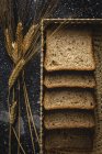 Top view of fresh homemade rye bread near knife in wicker basket and wheat spikes on table — Stock Photo