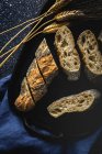 De cima de pão crosty apetitoso perto de picos de trigo e tecido escuro na mesa — Fotografia de Stock