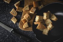 Pieces of crispy bread in bowl near wheat spikes on black textile in room — Stock Photo