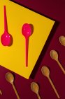 Overhead view of bright red and brown eco friendly spoons near yellow carton sheet — Stock Photo