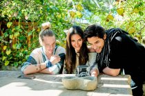 Junge fröhliche multiethnische Partner porträtieren sich mit Fotokamera am Tisch gegen Kletterpflanzen im Hof — Stockfoto