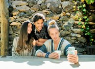 Молодые рады многонациональным партнерам, снимающим автопортрет на фотокамеру за столом против альпинистских растений во дворе — стоковое фото
