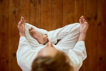Von oben ein anonymer Mann in weißen Kleidern, der Mudra-Geste mit den Händen macht, während er im Haus Yoga praktiziert — Stockfoto
