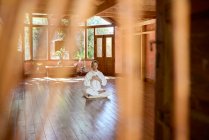 Молодий розумний чоловік босоніж, сидячи в позі лотоса на подушці з закритими очима практикує йогу на підлозі біля миски гонг і статуетки Будди — стокове фото