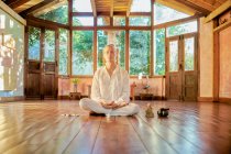 Joven hombre consciente descalzo macho sentado en pose de loto practicando yoga en el suelo cerca del gong bowl y la estatuilla de Buda - foto de stock