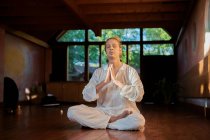 Joven hombre consciente descalzo macho sentado en pose de loto con los ojos cerrados practicando yoga en el suelo cerca del gong bowl y la estatuilla de Buda - foto de stock