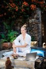 Jovem masculino surf internet no netbook enquanto sentado contra a estatueta de Buda e tigela gongo no pátio olhando para longe — Fotografia de Stock