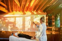 Curador praticando a técnica de cura da palma para cliente do sexo feminino deitado no sofá durante a prática espiritual para encher com harmonia e energia — Fotografia de Stock