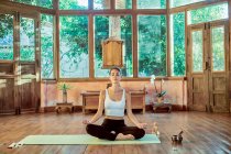 Jeune femme concentrée avec les yeux fermés pratiquant le yoga avec les jambes croisées près gong bol dans la maison — Photo de stock