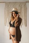 Donna incinta pensierosa in lingerie nera e cardigan che tocca la pancia e guarda giù in appartamento leggero durante il giorno — Foto stock