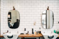 Table with assorted cosmetic products in bottles and dispensers between washstands under mirrors reflecting barbershop — Stock Photo