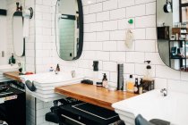 Table with assorted cosmetic products in bottles and dispensers between washstands under mirrors reflecting barbershop — Foto stock