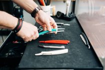 Crop anonymous beauty master with collection of razors and manual instruments at table in hairdressing salon — Fotografia de Stock