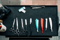 Top view of assorted scissors near straight razors with sharp metal blades on table in hairdressing salon - foto de stock
