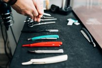 Crop anonymous beauty master with collection of razors and manual instruments at table in hairdressing salon — Stock Photo