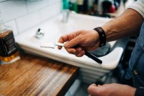 Crop unrecognizable male stylist holding straight razor with sharp blade in beauty salon in daytime — Stock Photo