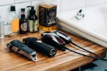 Collection of professional electric clippers near bottles of cosmetic products and washbasin in bathroom of barbershop - foto de stock