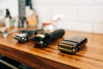 Collection of professional electric clippers near bottles of cosmetic products and washbasin in bathroom of barbershop - foto de stock
